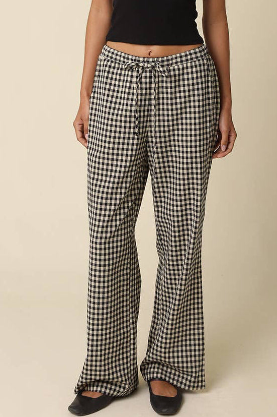 Woman wearing a black tank top and checkered pants against a beige background
