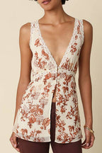 A model wearing a sleeveless cream vest with a rust-brown floral print and deep V-neckline, paired with dark brown wide-leg pants, standing against a solid beige background.