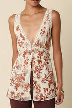 A model wearing a sleeveless, deep V-neck top with a brown and white floral toile pattern, paired with dark brown wide-leg pants, standing against a solid beige studio background.