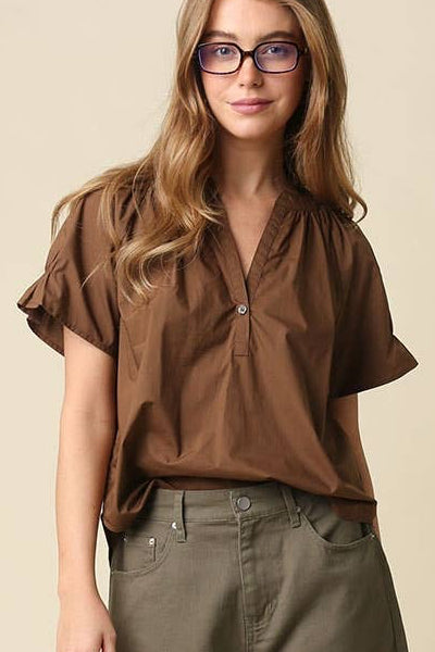 A woman modeling a brown short-sleeve blouse and olive green shorts against a plain beige studio background.