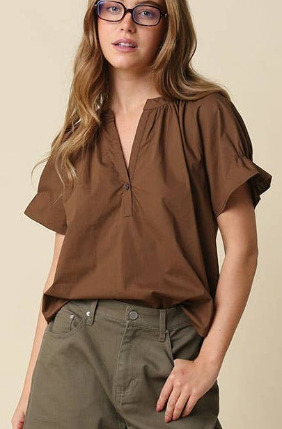 A woman modeling a brown short-sleeve blouse and olive green shorts against a plain beige studio background.