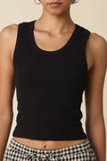 Woman wearing a black tank top and checkered pants against a beige background