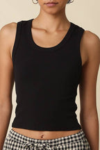Woman wearing a black tank top and checkered pants against a beige background