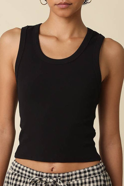 Woman wearing a black tank top and checkered pants against a beige background