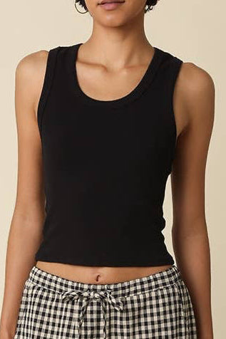 Woman wearing a black tank top and checkered pants against a beige background