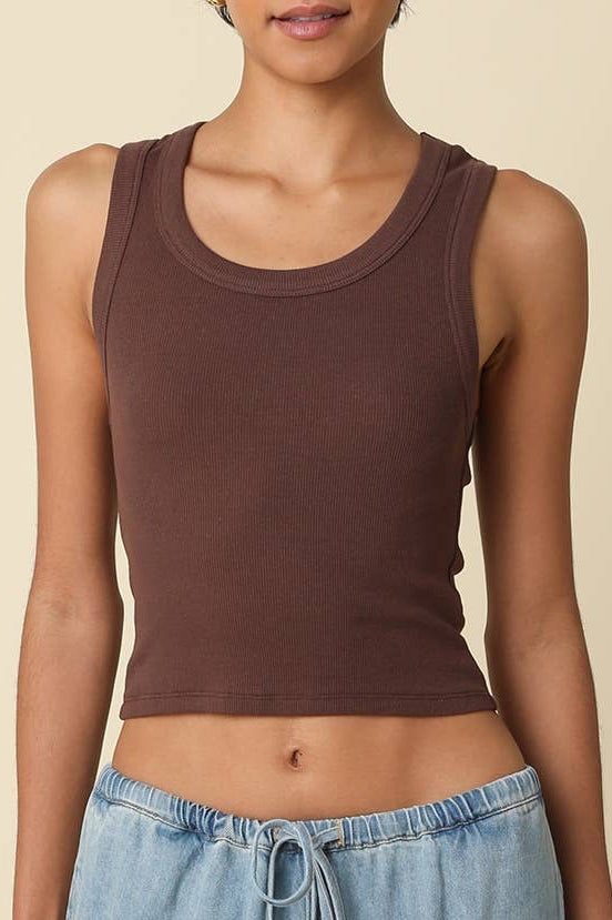 A woman modeling a dark brown ribbed tank top paired with light blue drawstring pants, set against a solid beige background.
