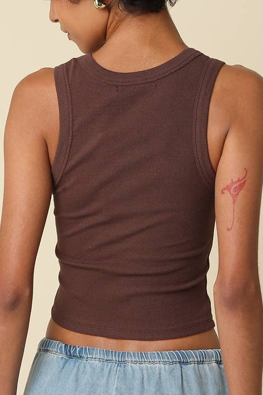Person wearing a brown tank top and blue jeans on a beige background