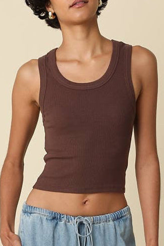 Woman wearing a brown tank top and blue wide-leg pants against a beige background