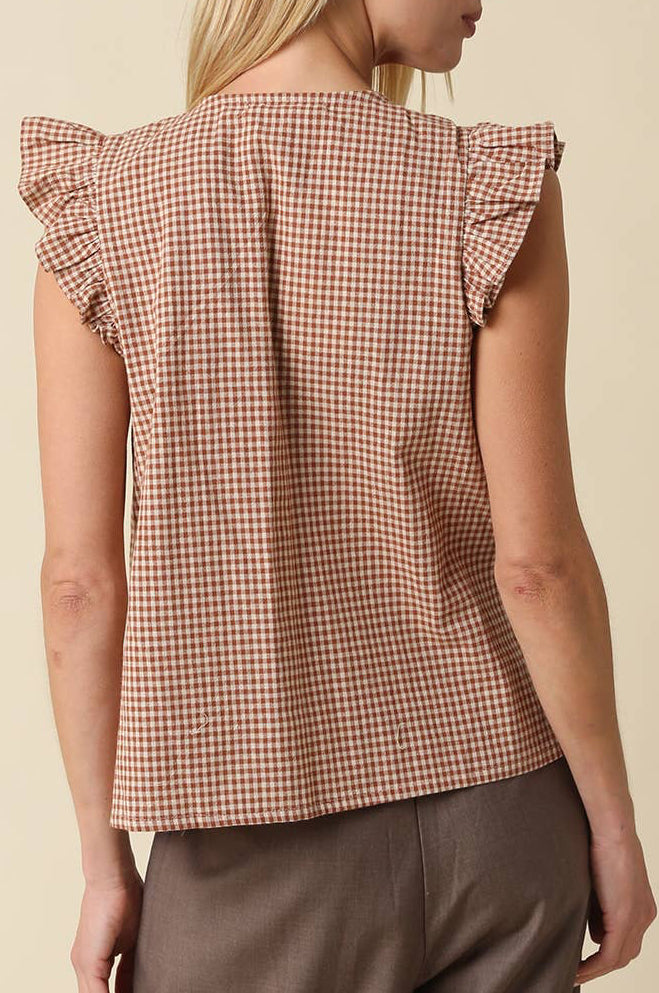 A woman shown from the back wearing a brown and beige gingham check top with ruffled cap sleeves, paired with brown trousers, against a solid beige background.