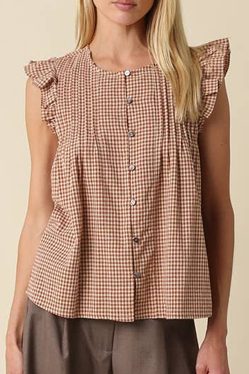 A woman modeling a sleeveless brown and beige gingham top with ruffled shoulders and a button front, paired with wide-leg taupe pants, against a plain beige studio background.