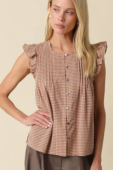 A woman modeling a brown and beige gingham sleeveless top with ruffled shoulders and button details, paired with wide-leg brown pants, against a solid beige studio background.