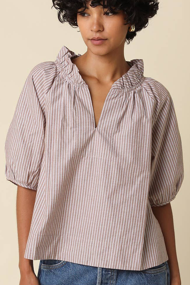 A woman wearing a short-sleeve puff-sleeve blouse with vertical pink and white stripes, paired with blue denim jeans, against a solid beige background.