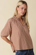 Woman wearing a brown and white checkered blouse with blue jeans on a beige background