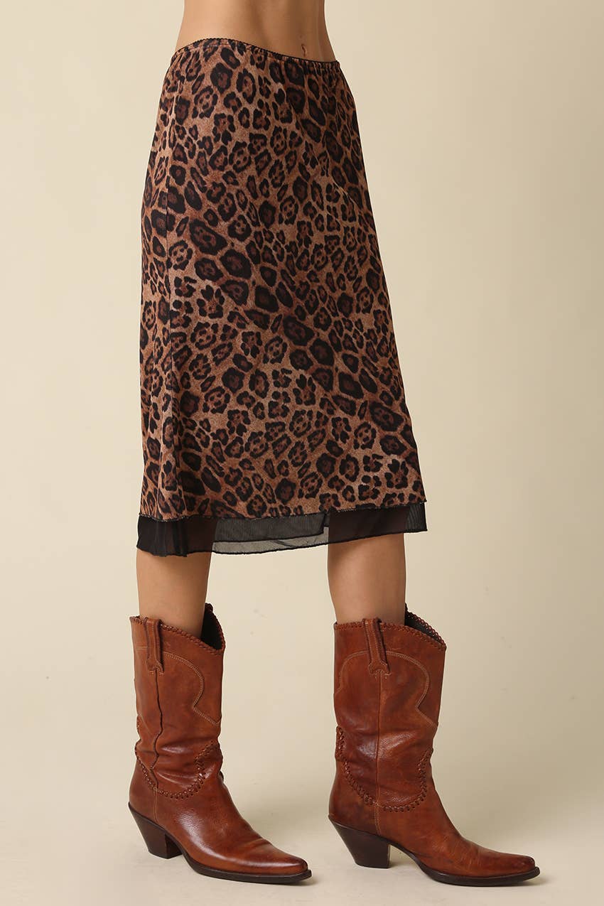 A leopard-print midi skirt in brown and black, styled with brown leather cowboy boots against a solid beige background.