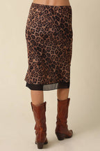 A leopard-print pencil skirt in brown and black, shown from the back on a model wearing brown leather cowboy boots against a light beige background.