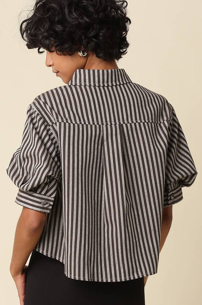 A woman shown from the back wearing a black and white vertically striped short-sleeve blouse with puff sleeves and black pants, against a plain beige studio background.
