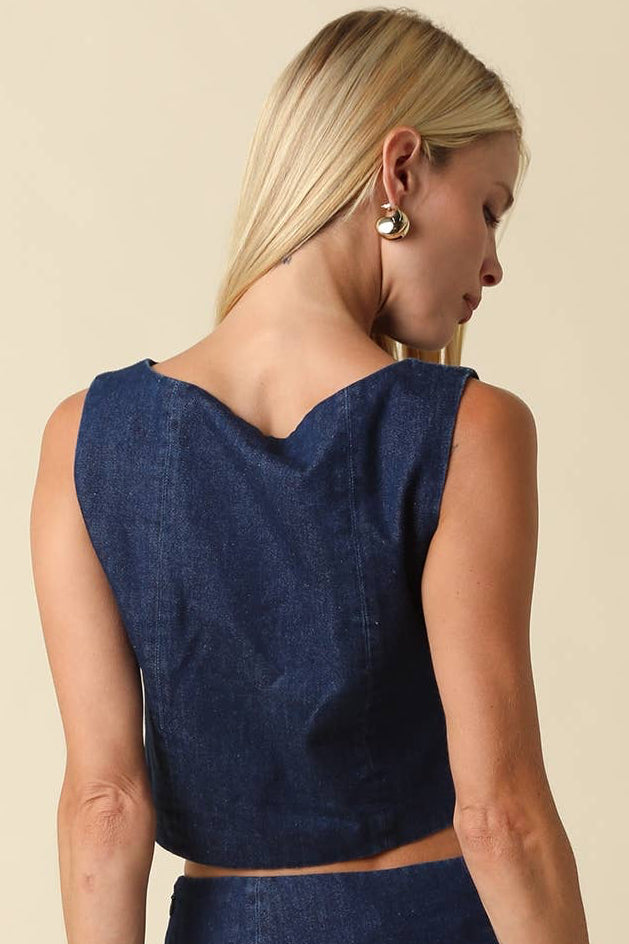 A woman shown from the back wearing a sleeveless dark blue denim-like crop top and matching skirt against a plain beige studio background.