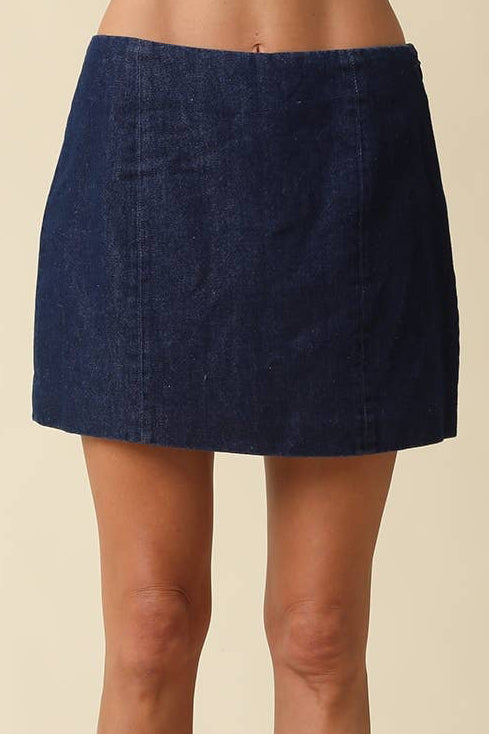 A model's lower body wearing a dark blue denim mini skirt and black leather cowboy boots, standing against a solid beige background.