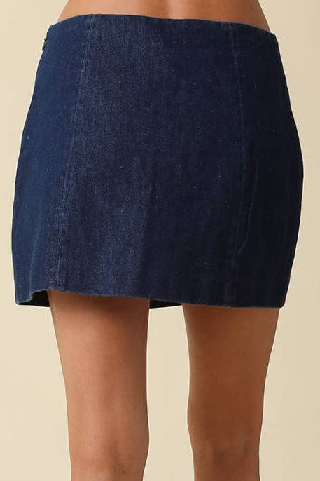 A person shown from the back wearing a dark blue denim mini skirt and dark gray knee-high heeled boots against a plain beige studio background.