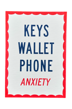 A square white card or sign with a red scalloped border, featuring the words 'KEYS WALLET PHONE' in dark blue and 'ANXIETY' in red, centered on a light gray background.