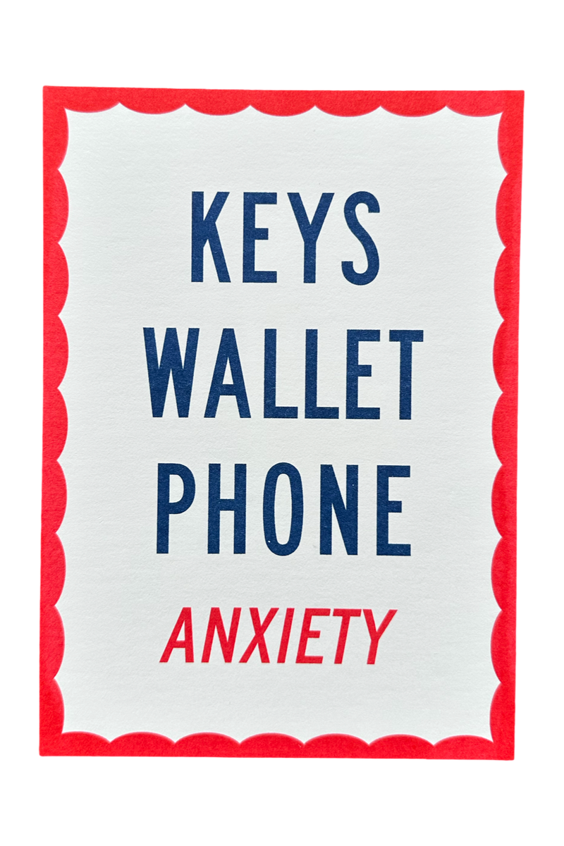 A square white card or sign with a red scalloped border, featuring the words 'KEYS WALLET PHONE' in dark blue and 'ANXIETY' in red, centered on a light gray background.