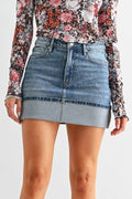 Woman wearing a floral top, denim skirt, and black knee-high boots on a white background