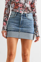 Woman wearing a floral top, denim skirt, and black knee-high boots on a white background