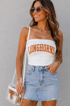A woman modeling a white strapless tube top with 'LONGHORNS' printed in orange across the chest, paired with a light blue denim mini skirt and a clear crossbody bag, set against a plain gray wall.