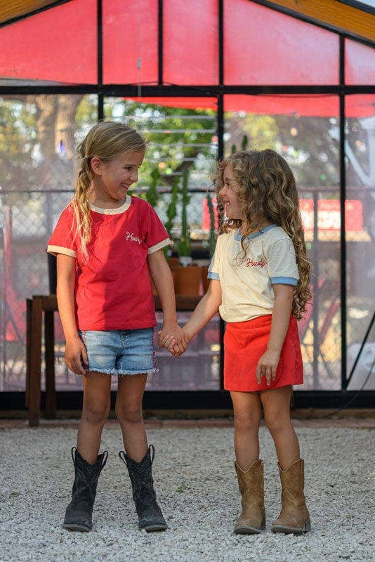 Two children holding hands in a greenhouse setting with plants and a transparent wall.
