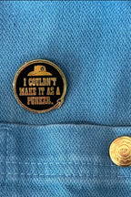 A round gold-tone enamel pin with a black center and text reading 'I COULDN'T MAKE IT AS A PUNKER.' is pinned to a blue denim jacket pocket, next to a matching blue denim snap button.