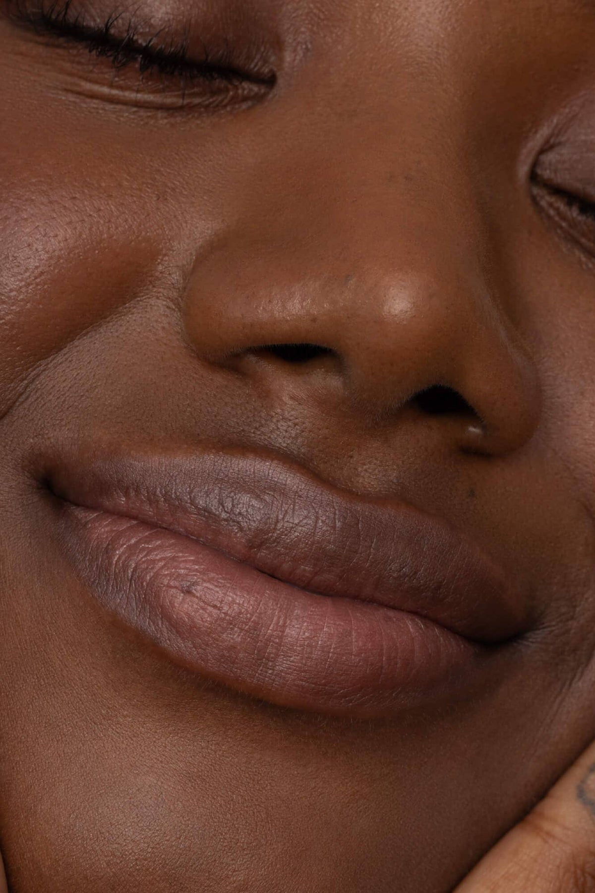 Close-up of a person with tattoos on their fingers touching their face.