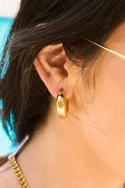 Close-up of a person wearing gold hoop earrings with a blurred background