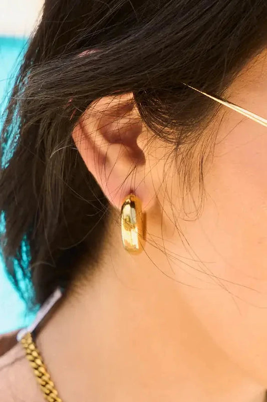 Close-up of a person wearing gold hoop earrings with a blurred background