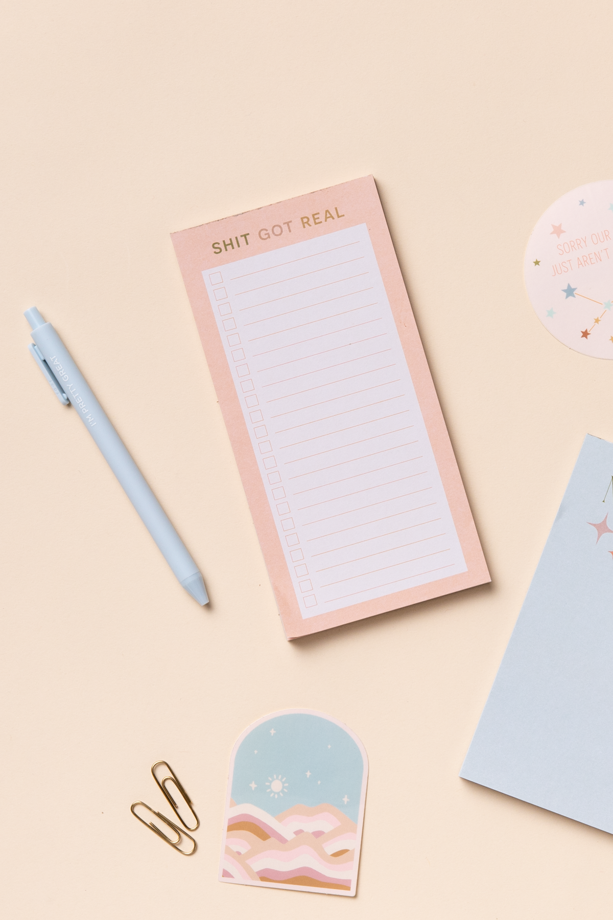 Extra small notepads with a pink and blue cover, alongside a pen, paper clips, washi tape, and a glue stick, all arranged on a beige background.