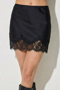 Person wearing a black lace skirt and black knee-high boots on a white background