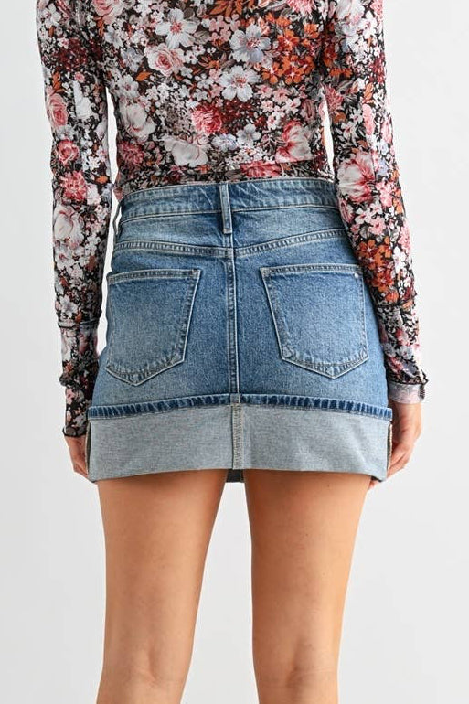 Woman wearing a floral blouse, denim skirt, and black knee-high boots on a light gray background