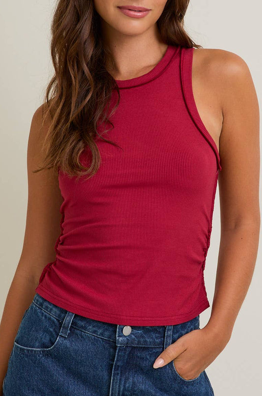 Woman wearing a red ribbed tank top and blue jeans against a neutral background