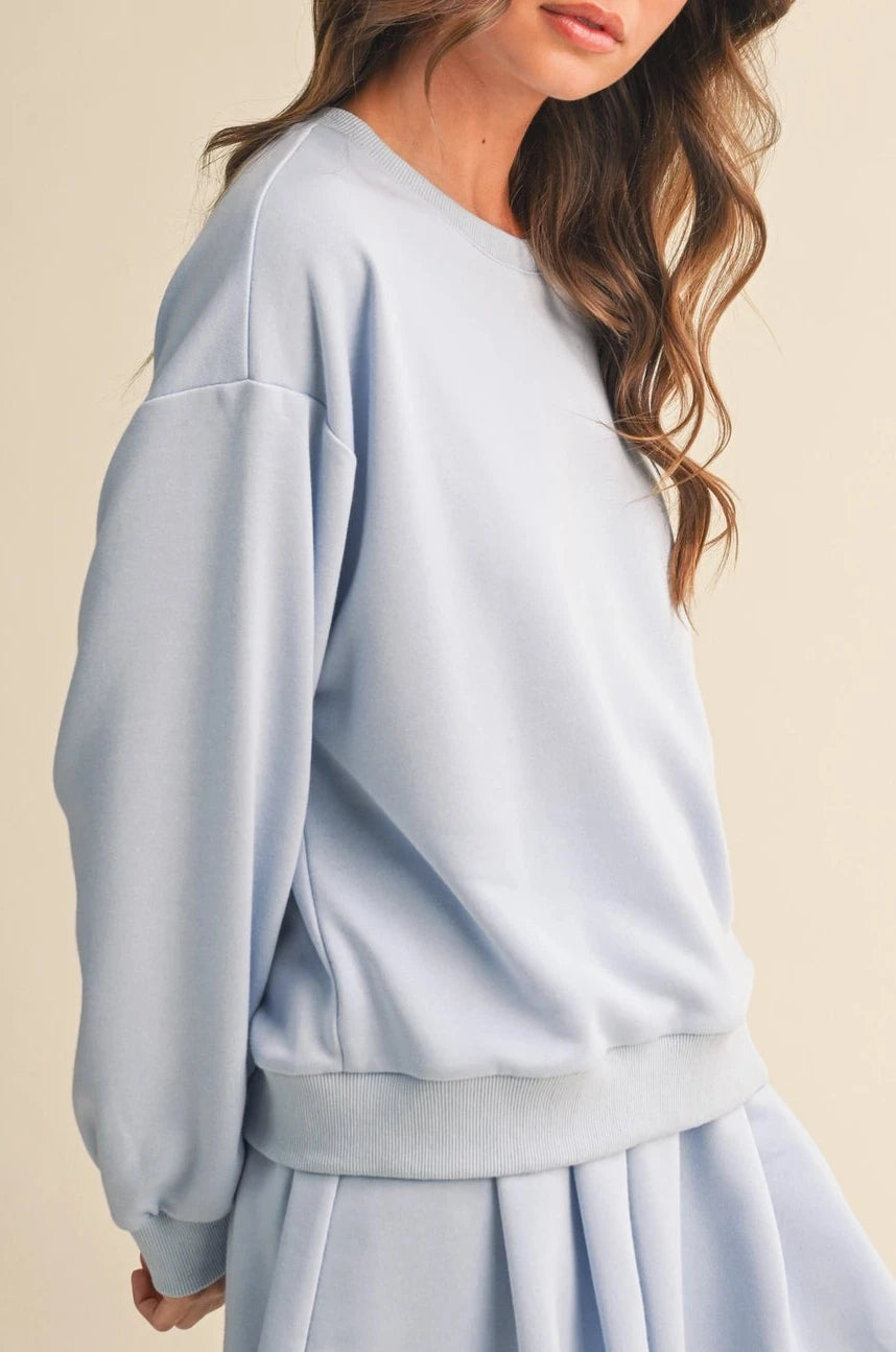Woman wearing a light blue sweatshirt and skirt set on a beige background