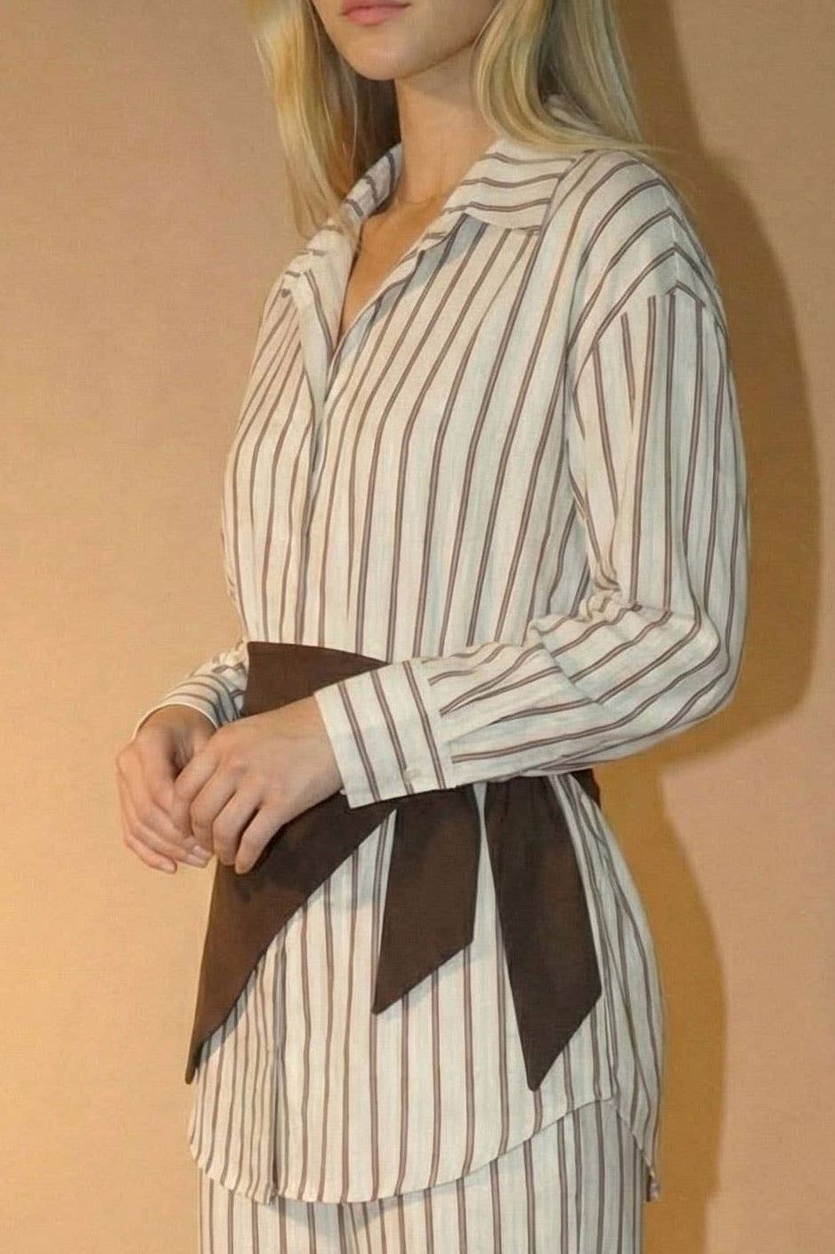 Woman wearing a striped outfit with a belt against a beige background