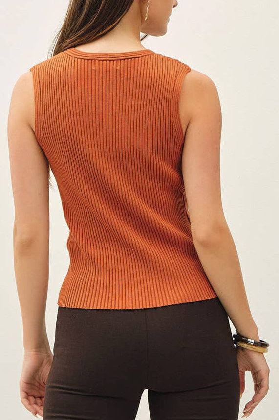A woman is shown from the back wearing a sleeveless orange ribbed knit top and dark brown cropped pants, paired with beige high-heeled sandals, against a plain white studio background.