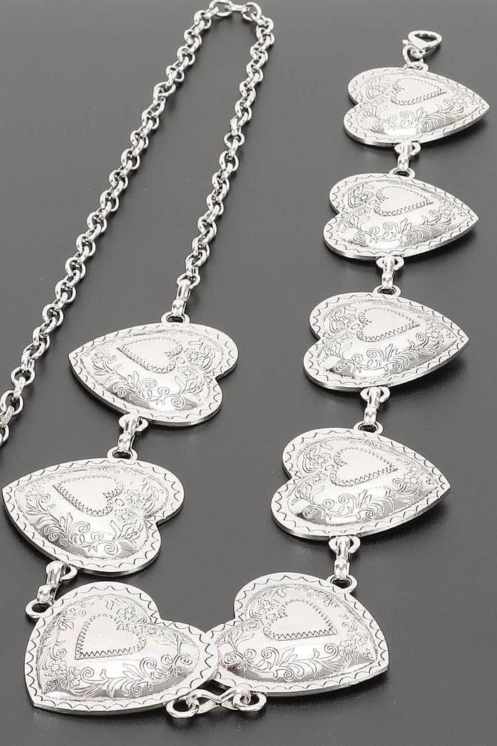 A silver heart-link chain necklace with multiple engraved heart charms, displayed on a dark gray background.