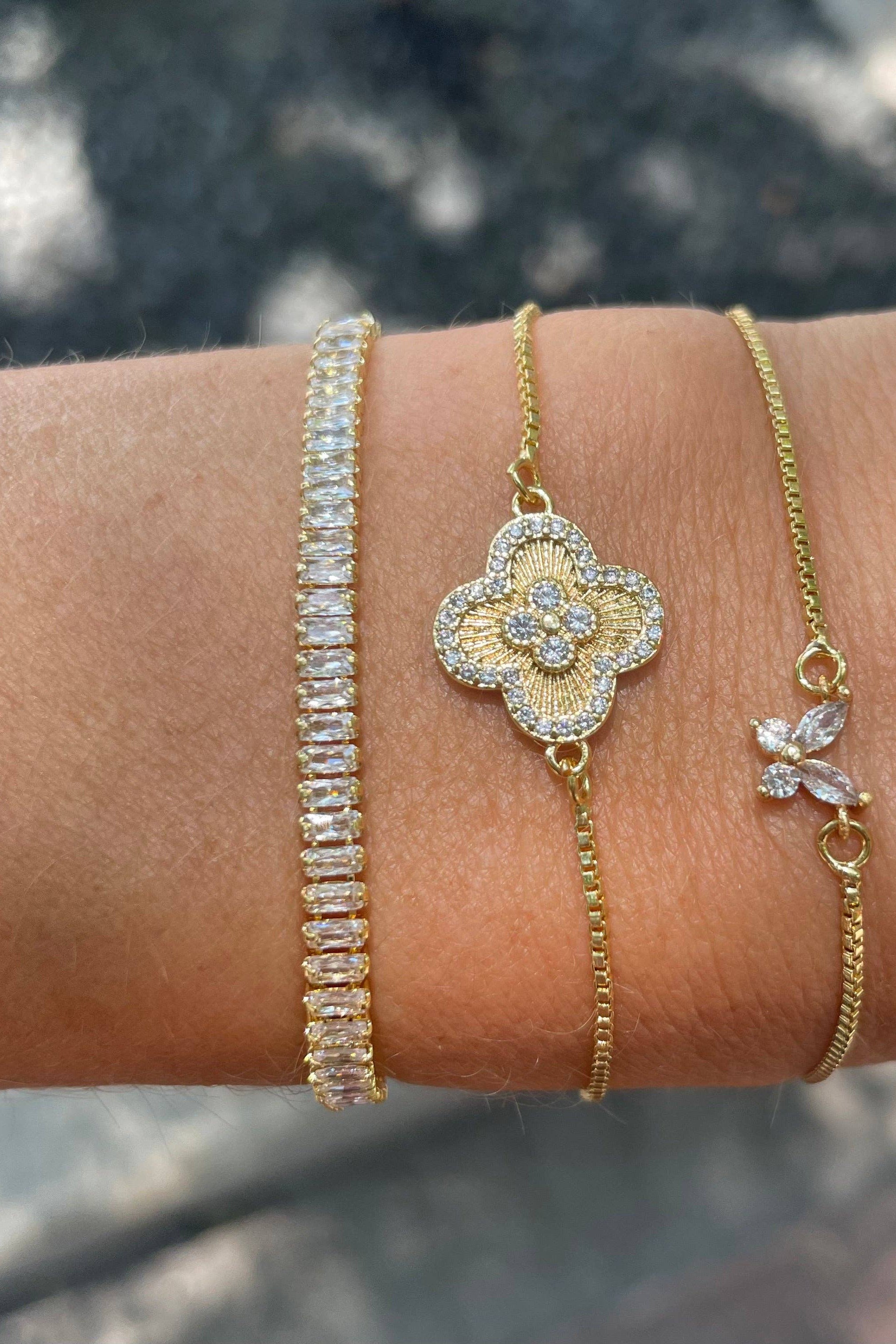Close-up of a wrist wearing three gold bracelets with intricate designs.