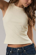 Woman wearing a beige tank top and blue jeans on a gray background