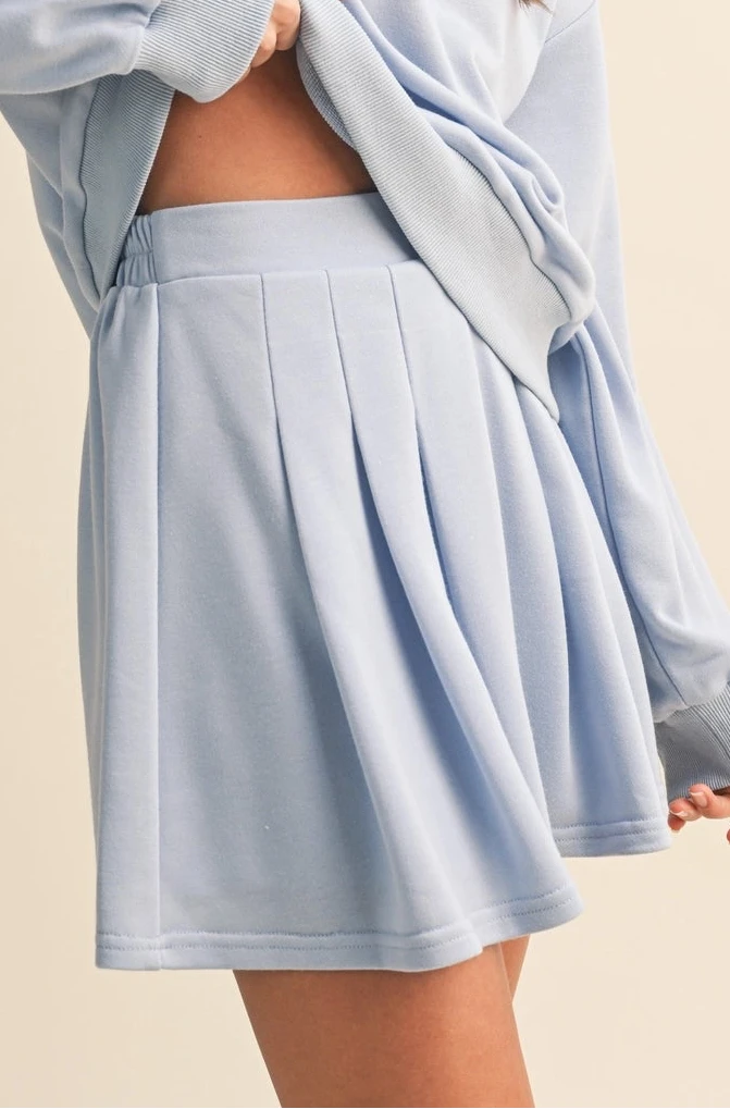 Woman wearing a light blue oversized sweatshirt and skirt set on a beige background