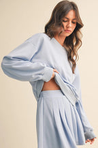 Woman wearing a light blue oversized sweatshirt and skirt set on a beige background
