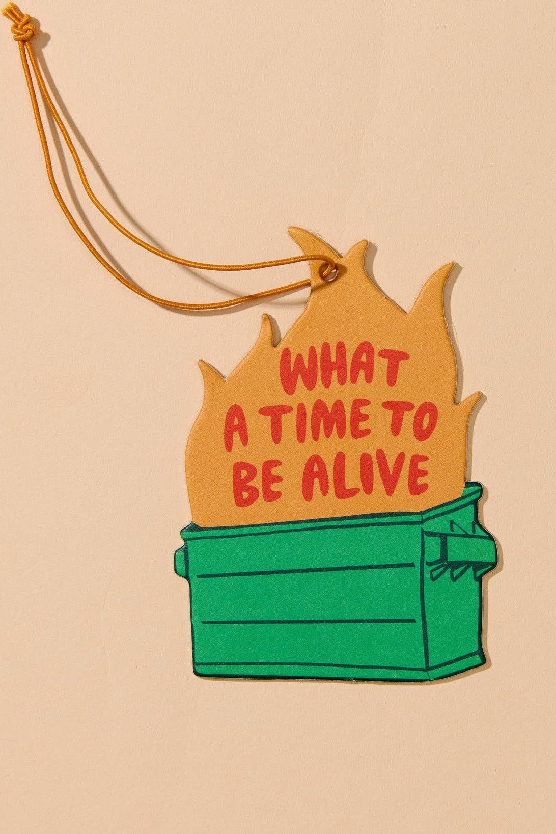 A die-cut enamel pin or sticker featuring a green dumpster on a beige background with orange flames and the text 'WHAT A TIME TO BE ALIVE' in red. A thin orange hanging string is attached at the top.