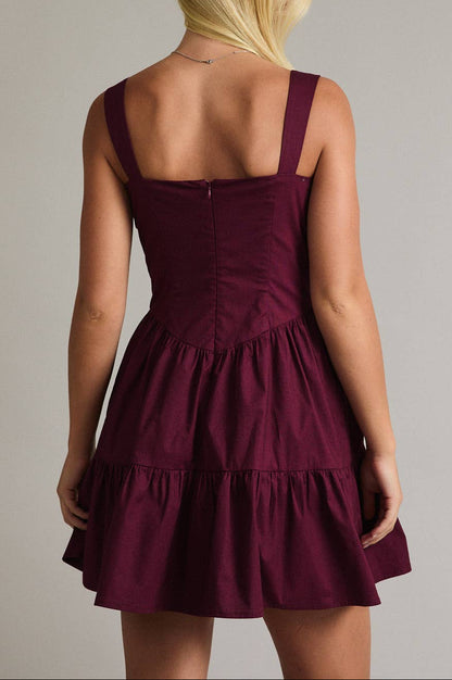 Woman wearing a burgundy dress with thin straps on a plain background