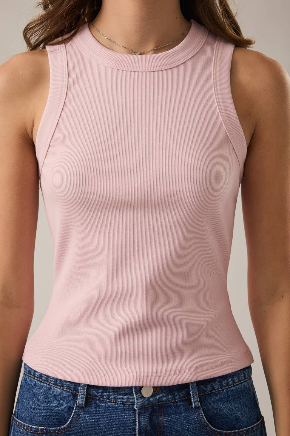 Person wearing a pink sleeveless top and blue jeans on a neutral background
