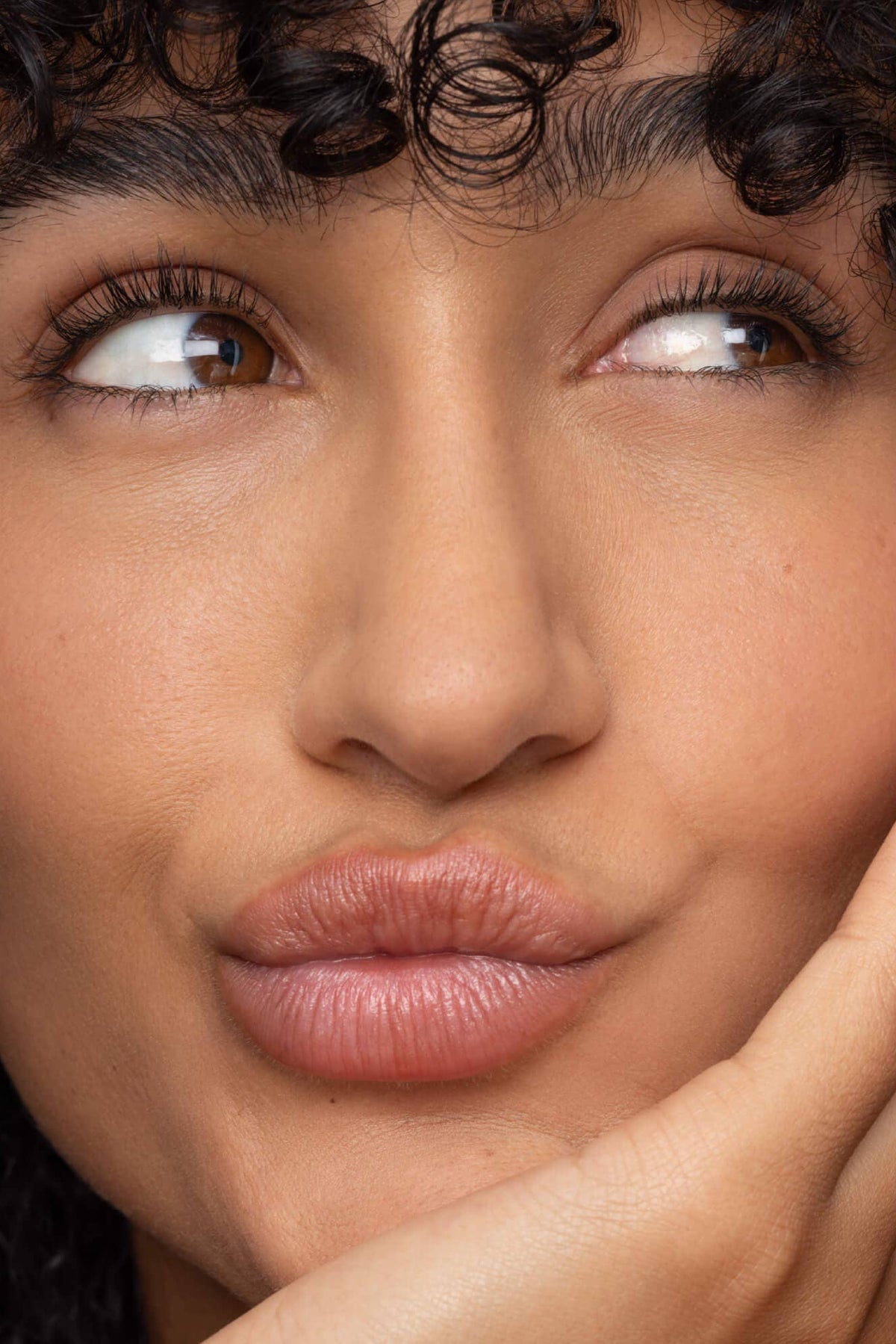 Close-up of a woman with curly hair and hand on face