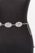 A silver western-style belt with three oval engraved medallions and a hanging chain, displayed on a black mannequin torso against a white background.